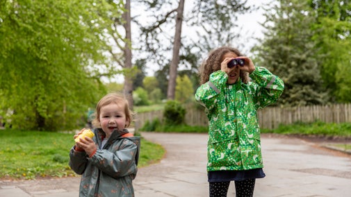 Two children outdoors, the eldest looking through a pair of binoculars